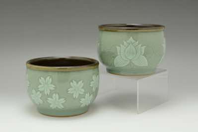 These matcha tea bowls, which can also function as soup bowls, were hand-thrown and hand-carved with traditional Asian patterns.  The patterns include lotus flowers and cherry blossoms.  Because celadon is a crackle glaze, dark tenmoku glaze is used for the interior of the bowl instead.  The tea bowl is used for preparing the tea by whisking matcha powder and hot water as well as for drinking directly from it.