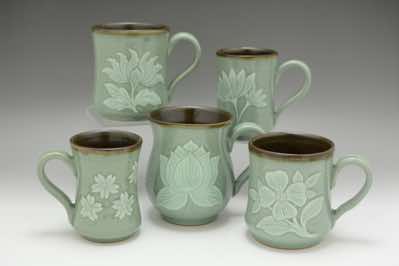 These coffee mugs were hand-thrown and hand-carved with traditional floral patterns.  The patterns include peonies, water lilies, cherry blossoms, lotus flowers and dogwood flowers.  They come in 3 sizes - small (300ml or 10oz), medium (450ml or 15oz) and large (600ml or 20oz).  Because celadon is a crackle glaze, dark tenmoku glaze is used for the interior of the mug instead.   